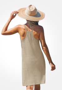 Beige ärmelloses Kleid mit lockerer Passform, Schulterträgern und strukturiertem Stoff. Kombiniert mit einem breitrandigen Strohhut, der einen einfachen, lässigen Stil zeigt.