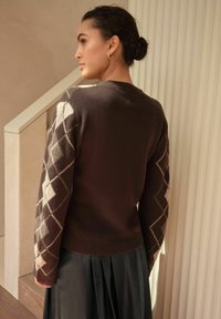 Brown sweater with diamond pattern in cream and light gray on sleeves. Knit texture, ribbed neckline, and hem, paired with a pleated black skirt.