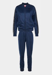 Survêtement bleu marine en polyester avec veste à fermeture éclair intégrale, poignets et taille côtelés, pantalon fuselé et bandes logo sur les manches.