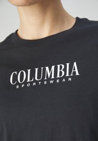 Svart bomullströja med rund halsringning, prydd med en vit tryckt logotyp som tydligt visar "COLUMBIA SPORTSWEAR" på framsidan.
