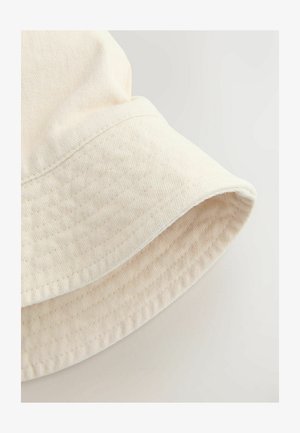 Világosbézs texturált anyagból készült vödör kalap, széles, enyhén lógó karimával és finom varrási részletekkel.