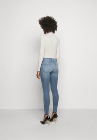 Jeans ajustados azules con una cintura alta, hechos de mezclilla. Combinados con una blusa ajustada de manga larga en color crema y zapatos de tacón negros con punta afilada.