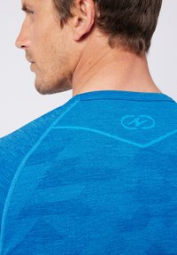 Maglietta sportiva blu con un motivo testurizzato e un collo curvo, con cuciture a contrasto e un logo sul retro.