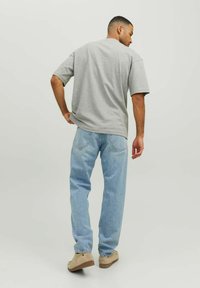 Sivý tričko s krátkym rukávom skombinované s svetlomodrými džínami. Tkanina vyzerá mäkká a uvoľnená s rovnými nohavicami. Béžové topánky dotvárajú vzhľad.