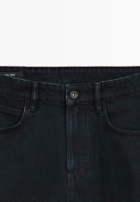 Jeans in denim nero con zip, chiusura a bottone in metallo, tasche frontali e dettagli di cucitura sottili. Vita piatta. Texture liscia.