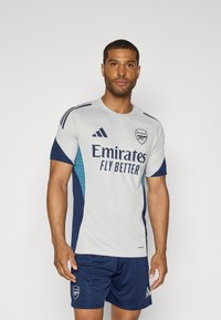 Grijze en marineblauwe sporttruid met korte mouwen, voorzien van het logo "Emirates Fly Better" en Adidas strepen. Gemaakt in combinatie met marineblauwe shorts.