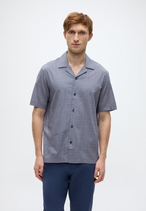 Πουκάμισο με κοντά μανίκια σε ναυτικό μπλε με γεωμετρικό σχέδιο, κατασκευασμένο από ελαφρύ ύφασμα. Διαθέτει γιακά τύπου καμπ και σκουρόχρωμα κουμπιά.