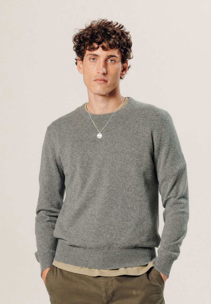 Grauer Wollpullover mit Rundhalsausschnitt, gerippten Bündchen und Saum, über einem beigen Hemd getragen. Bietet eine dezente Textur und eine lockere Passform.