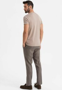Beige tričko s krátkým rukávem v kombinaci se šedými kalhotami rovného střihu a hnědými šněrovacími botami. Jednoduchý design, hladká textura a neutrální barvy.