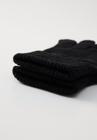 Svart strikkede hansker brettet pent. Laget av myk ull, med ribbestrikkede mansjetter og en jevn tekstur. Fem-fingerdesign uten ekstra detaljer.