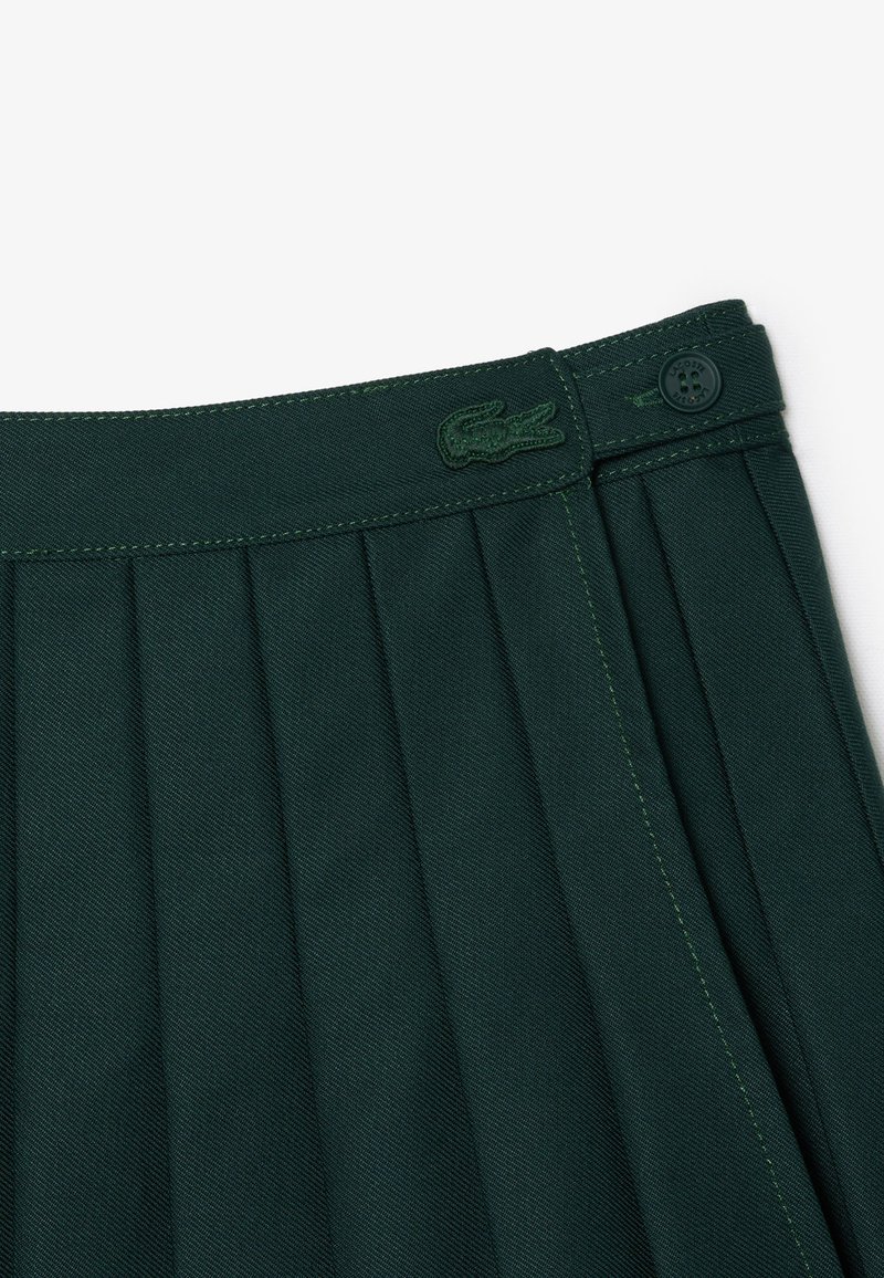 Grüne, gefaltete Rock aus einem strukturierten Stoff, mit gesticktem Logo am Bund und kontrastierenden grünen Nähten.