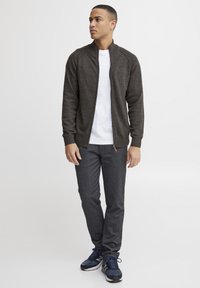Cárdigan gris oscuro con cremallera sobre una camiseta blanca, combinado con pantalones ajustados gris oscuro y zapatillas deportivas azul marino. Tejido texturizado con puños acanalados.