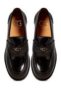 Black leather loafers with a glossy finish, featuring a strap and gold logo accent, rounded toe and textured detailing on the upper.