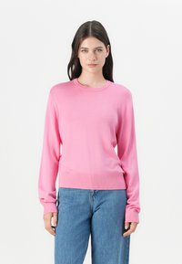 Roza jopica dolgega rokava iz lahkotnega pletenega materiala, z okroglim izrezom, rebrastimi manšetami in robom, v kombinaciji s ohlapnimi modrimi kavbojkami.