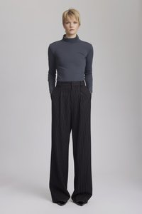 Grå tröja med hög hals som passar nära kroppen, kombinerat med svarta randiga vida byxor med hög midja och en slät textur. Vassa svarta klackar fulländar looken.