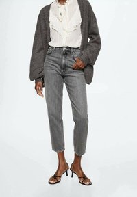 Jeans grises de cintura alta con forma ajustada, con un lavado desgastado y diseño de cinco bolsillos, combinados con una blusa blanca con volantes y un cárdigan oscuro.