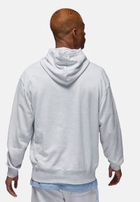Lys grå fleece hoodie med snoretræk i hætten, afslappet pasform og ribbede manchetter. Viser et lagdelt look over en blå skjorte nedenunder.