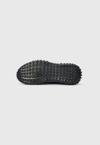 Black rubber shoe sole with a textured surface featuring round grip patterns and a curved shape, designed for traction and durability.