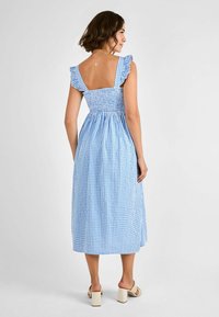 Vestido midi de cuadros azules con tirantes con volantes, corsé fruncido y falda fluida. Presenta un escote en la espalda y una tela texturizada.