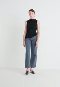 Top negru fără mâneci, cu detalii pliate pe lateral, asociat cu blugi din denim albastru, cu talie înaltă și ușor conici, purtați cu pantofi cu toc închis.