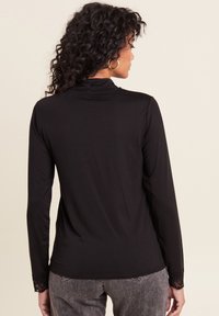 Schwarzes langärmliges Shirt mit tailliertem Design, das Spitzenakzente an den Manschetten und einen hohen Kragen aufweist. Weicher Stoff.