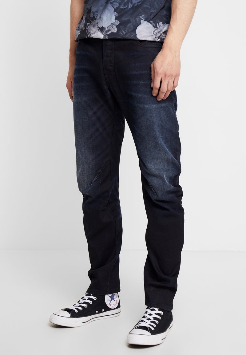 Mörkblå denimjeans med slim fit, som har subtila blekningar, fyra fickor och en klassisk femfickorsdesign. Bärs med svarta canvas-sneakers.