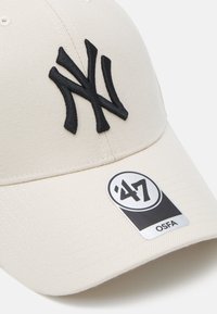 Beige színű baseball sapka fekete hímzett "NY" logóval, 47-es márkájú címke, texturált anyag, ívelt napellenző, állítható méret.