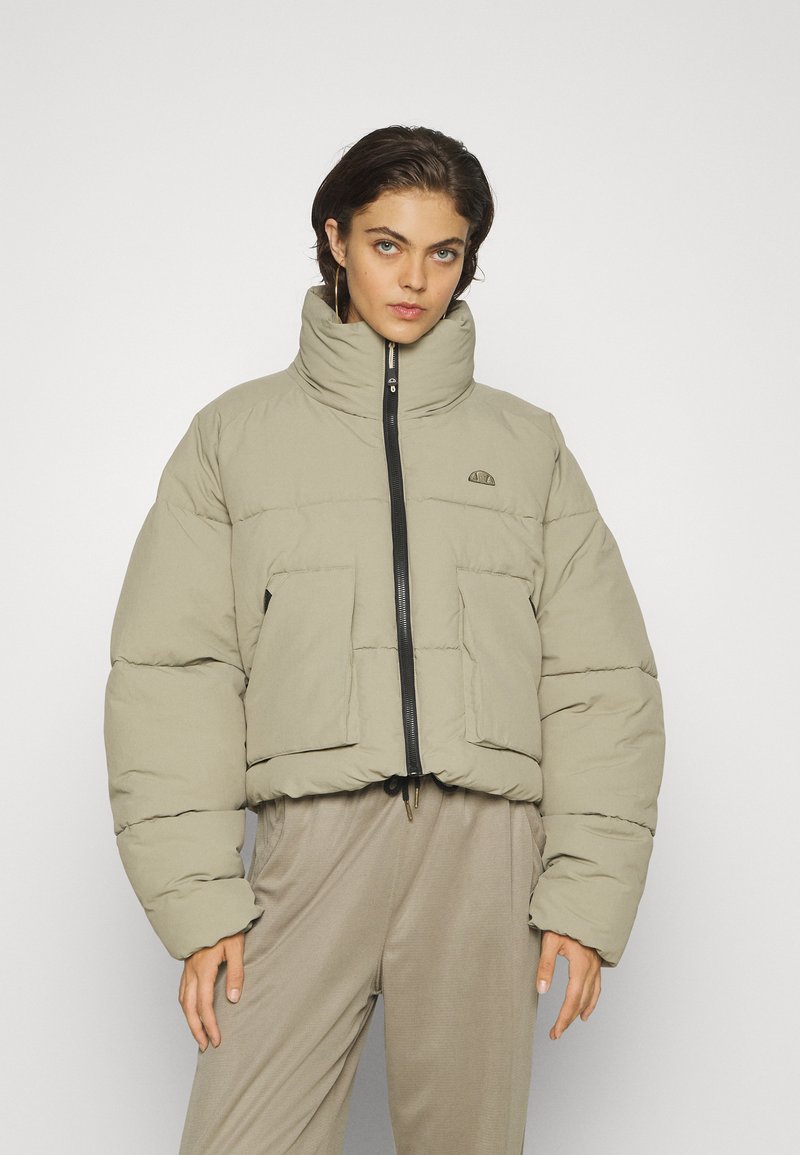 Puszysta beżowa kurtka z wysokim kołnierzem, czarnym zamkiem błyskawicznym i dwiema przednimi kieszeniami. Teksturowana tkanina i sznurek do regulacji na dole dla lepszego dopasowania.