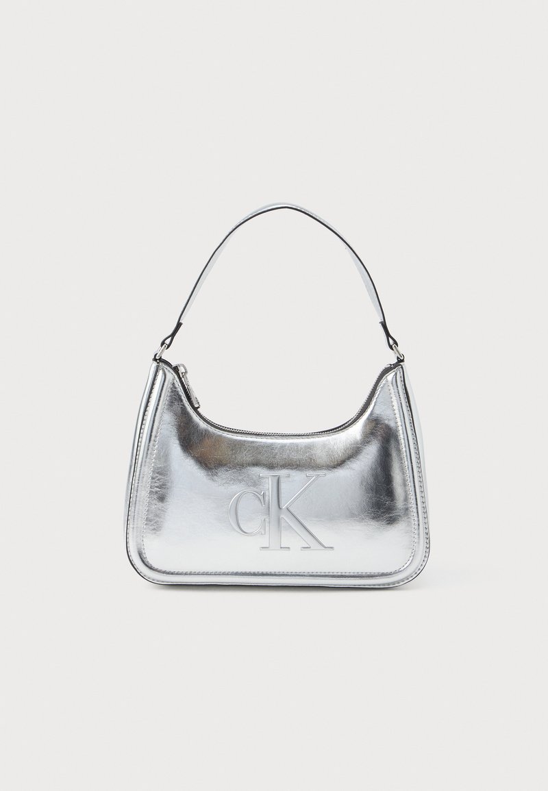 Sølvmetallic håndtaske med en buet form, lynlåslukning og skulderrem. Har et præget "CK" logo på fronten.