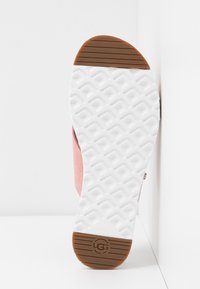 De buitenzool van de schoen heeft een roze suède bovenwerk en een witte rubberen zool met een gestructureerd grippatroon, verfraaid met een bruine rubberen sectie aan de hiel.