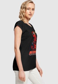 Melna īsām piedurknēm t-kreklā ar krāsainu Deadpool grafiku vidū. Audumam ir gluda tekstūra, kas paredzēta ikdienas valkāšanai.