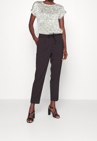 Ljusgrön mönstrad topp med zebra-ränder, tillsammans med svarta smala byxor med dragsko i midjan och eleganta svarta klacksandaler.