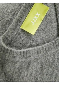 Nahaufnahme des Kragens eines grauen Strickpullis mit einem gelben Stoffetikett, auf dem "JJXX" steht, das innen eingenäht ist.