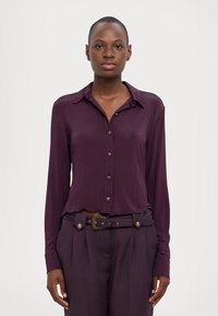 Camicia a maniche lunghe, con bottoni, in tessuto viola intenso. Presenta un colletto classico, bottoni frontali e un orlo leggermente accorciato.