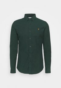 Camicia button-up verde scuro con maniche lunghe, caratterizzata da un colletto classico, bottoni scuri e un piccolo logo giallo sul lato sinistro del petto.