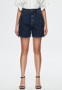 Tmavě modré džínové šortky s vysokým pasem, vybavené předními kapsami, zavíráním na knoflík a prošitým lemem. Doplněné černými sandály na podpatku.