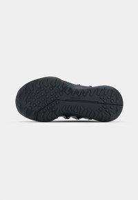 Black athletic shoe sole with textured rubber for grip, featuring triangular and rectangular patterns. Traxion label visible on the side.