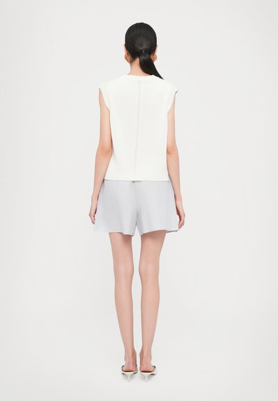 Top bianco a maniche corte con una texture a maglia, abbinato a pantaloni corti grigi chiari. L'outfit presenta un design semplice e casual con una costruzione senza cuciture.