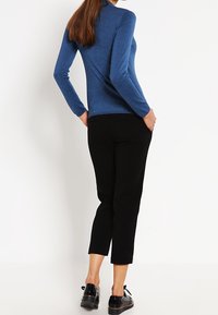 Top azul de manga larga combinado con pantalones cortos negros. El top tiene una textura suave, mientras que los pantalones están cortados a medida con un ajuste entallado. Unos zapatos negros completan el look.