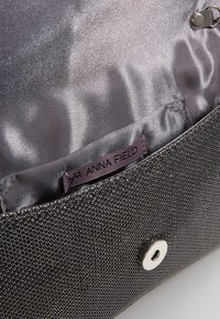 Černá texturovaná kabelka s lesklým interiérem. Obsahuje magnetické zapínání, vnitřní štítek s nápisem "ANNA FIELD" a hladkou podšívku.