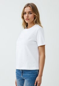 Witte t-shirt met korte mouwen en een ronde hals, met subtiele sprankelende details op de voorkant en een relaxte pasvorm.