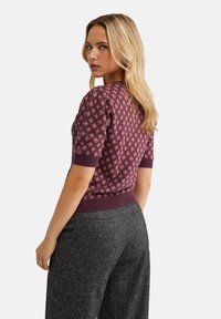 Stickad kortärmad tröja i mörkröd med ett geometriskt mönster, med en ribbad nederkant. Kombinerad med mörkgrå strukturerade byxor.