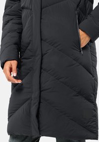 Black puffer coat with diagonal quilted texture, zippered pocket, and a smooth, water-resistant fabric. Mid-length design with a high collar.