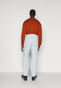 Pánský outfit skládající se z hnědočervené košile s dlouhým rukávem a světle modrých kalhot, s hladkým textilním povrchem a zúženým střihem. Klasické černé boty.