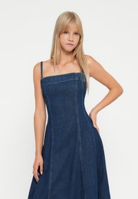 Donkerblauwe denim jurk met een aansluitend lijfje, vierkante halslijn en dunne schouderbandjes, voorzien van verticale naden en een uitlopende rok.