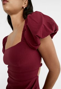 Bordeaux-farbenes, tailliertes Kleid mit puffärmel, quadratischem Ausschnitt und seitlichen Ausschnitten. Glattes Material mit gerafften Details an den Schultern.
