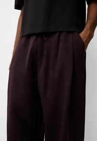 Pantalones holgados de un oscuro color burdeos con una textura suave, que cuentan con bolsillos laterales y una cintura con cordón, combinados con una blusa negra de manga corta.