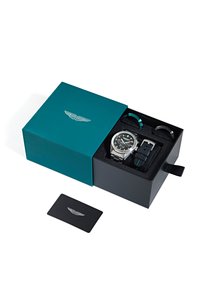Ezüst óra fekete számlappal és rozsdamentes acél szíjjal, egy zöldeskék dobozban, emboszált logóval és extra fekete, mintás szíjakkal.