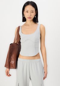 Grå cropped topp med en tettsittende design og brede stropper, sammen med lysegrå joggebukser og en brun lær tote bag.