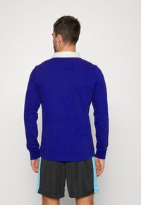 Kungsblå långärmad skjorta med vit krage, ribbat mönster och rak skärning, matchad med mörka shorts med ljusblå accenter.